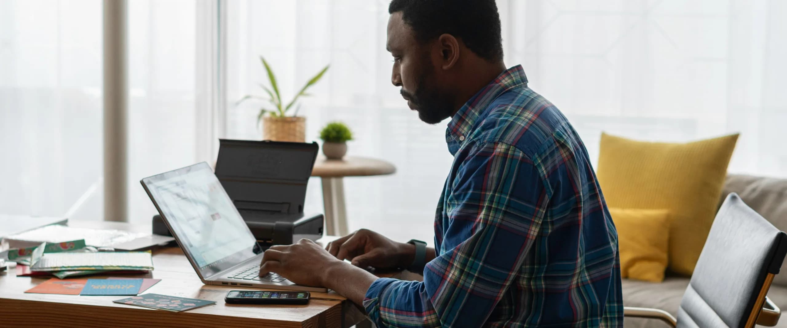 A solo operator working at a laptop with notebooks and printed papers spread across the desk.